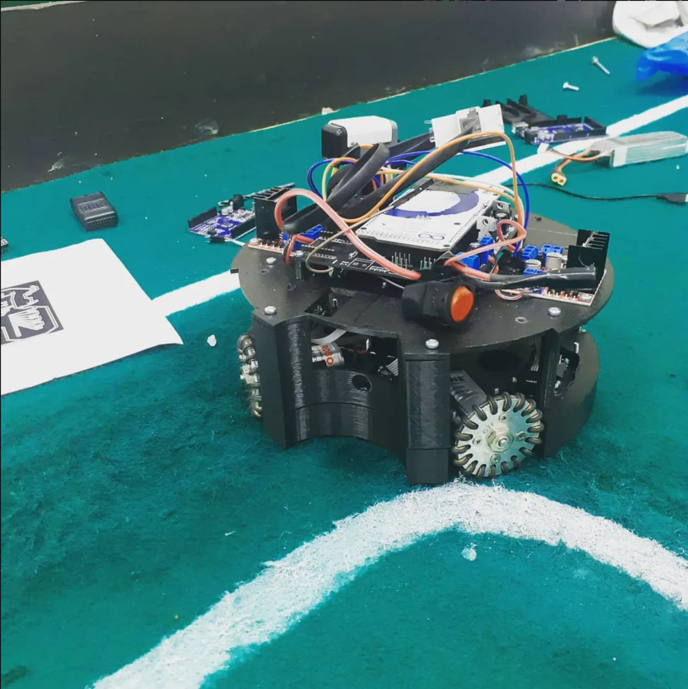 The omnidirectional soccer robot on the competition field, control boards and wiring exposed